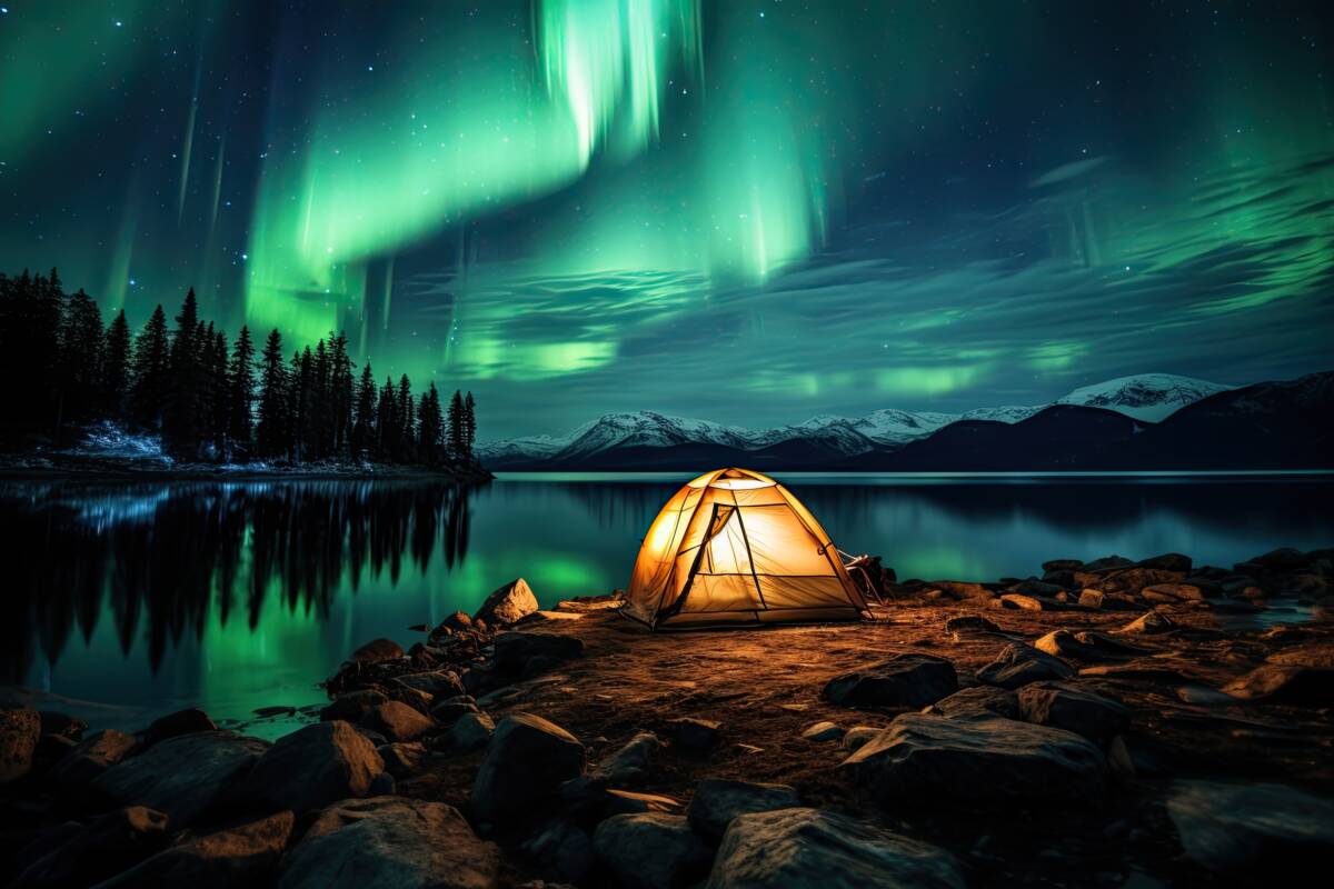 A tent glows under a night sky full of stars and aurora
